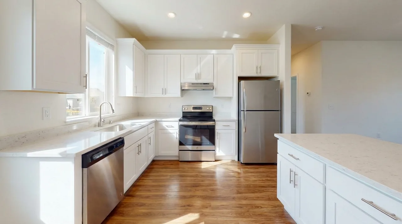 Record each appliance's make, model, and existing wear at move-in A clean, empty, move-in-ready rental kitchen with stainless steel refrigerator, oven, and dishwasher and spotless light countertops, photographed at handover